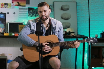 A musician holds a guitar while wearing Finalace headphones in front of a smartphone on a tripod